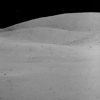 Лунный модуль «Орион» вдали (слева внизу). Видна скала House Rock, огромный валун на краю кратера Северный Луч (чуть выше и правее центрального перекрестия). Снимок сделан Чарли Дьюком со Station 4 на камеру с 500-мм объективом