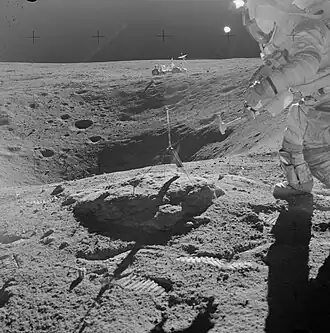 Янг готовится молотком отколоть кусок от валуна на краю кратера Плам